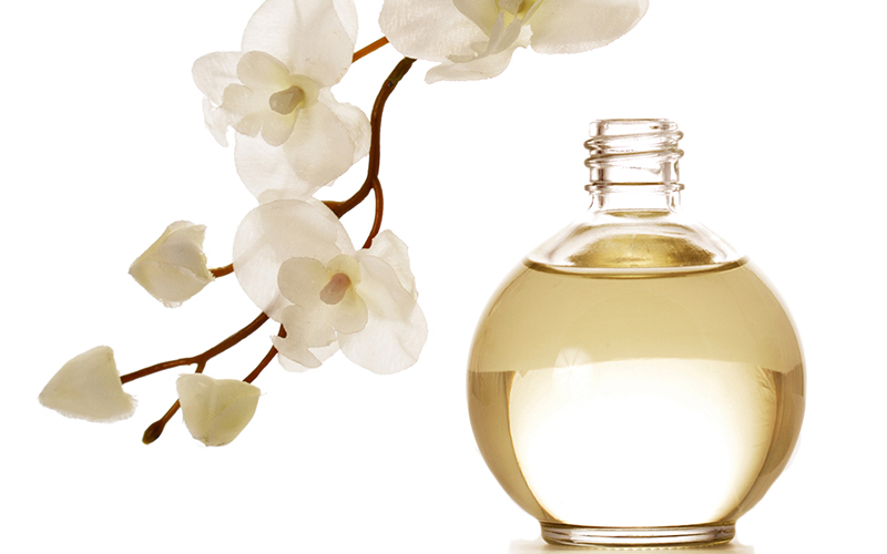 A perfume bottle with a sprig of orchids hanging over it
